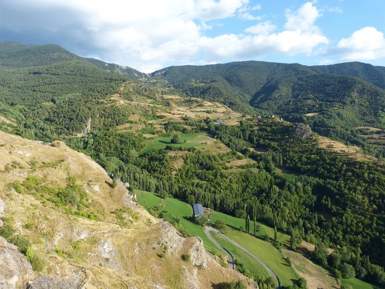 Valle del Pirineo visto desde arriba, con casas de piedra, prados y bosque